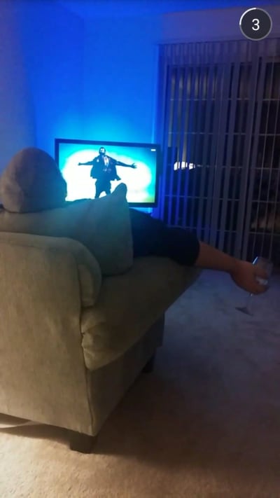 photo of relaxed man sitting on couch with wine watching Kanye west music video